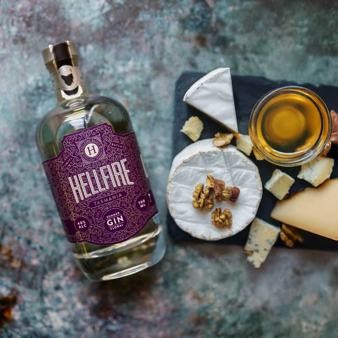 A bottle of Hellfire Bluff Distillery gin beside a gourmet Tasmanian cheese platter, representing the art of pairing premium liqueurs with local Tasmanian cuisine.